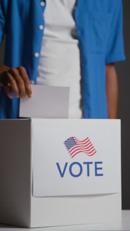 Vertical-Video-Close-Up-Shot-Of-Man-Casting-Vote-Into-Election-Ballot-Box-Against-Black-Background